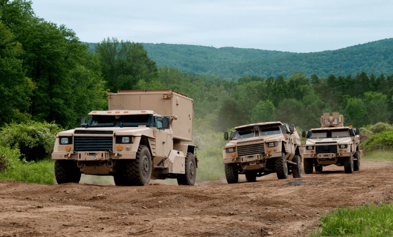 Prototype military vehicles driving through a mountain landscape that were made by RCO Engineerings defense manufacturing services